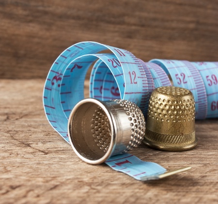two thimble and measuring tape on a wooden backgroundの写真素材