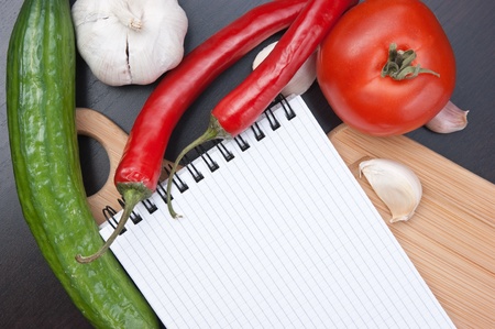 notebook for cooking recipes and vegetables on a cutting boardの写真素材