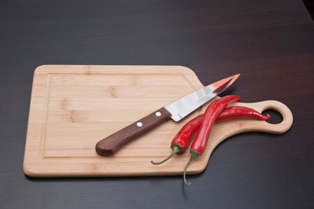 Two red chili peppers and knife on the kitchen tableの写真素材