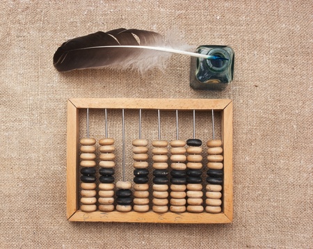 old glass inkwell with a quill pen and abacus on a wooden table