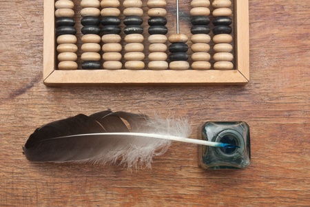 old glass inkwell with a quill pen and abacus on a wooden tableの写真素材