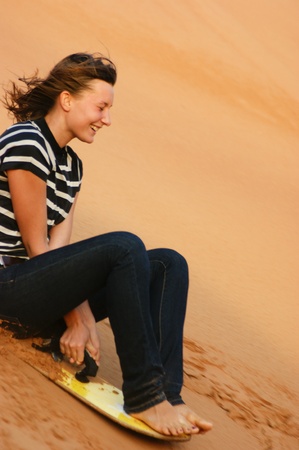 teen girl riding on the sand dunes sandboard in the Arabian desertの写真素材