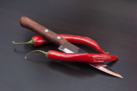 Two red chili peppers and knife on the kitchen tableの写真素材