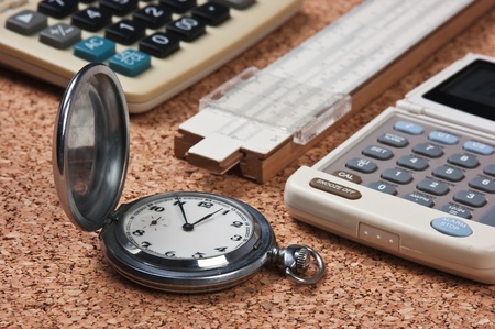 pocket watch,  calculator  and slide rule on a cork boardの写真素材