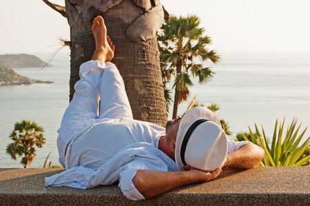 A young man in a white suit lies on the waterfrontの写真素材
