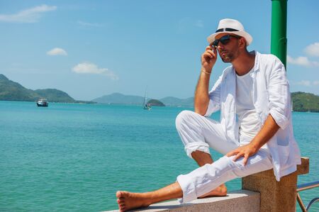 A young man in a white suit sits on the waterfrontの写真素材