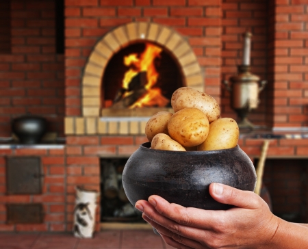cast iron pot with a potato in the hands in Russian cuisine  with an oven and a burning fireの写真素材