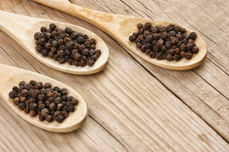 Black pepper in wooden spoon on the old board