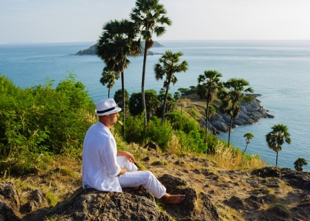 a young man sitting on a rock and looking at the sunset of Phuketの写真素材