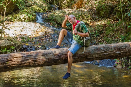 Travelling man sitting on a log near the river in the jungleの写真素材