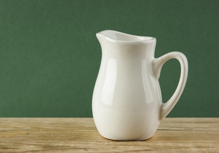 White jug on old wooden table over green backgroundの写真素材