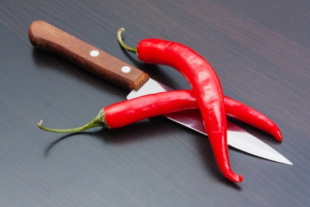 Two red chili peppers and knife on the kitchen tableの写真素材