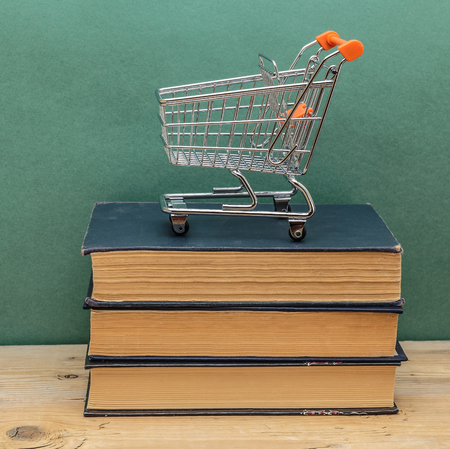 stack of old books on a wooden shelf and shopping cartsの写真素材