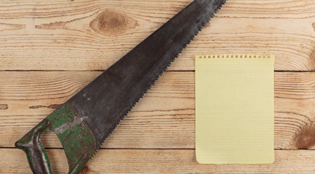 old saw and a piece of notebook on wooden backgroundの写真素材