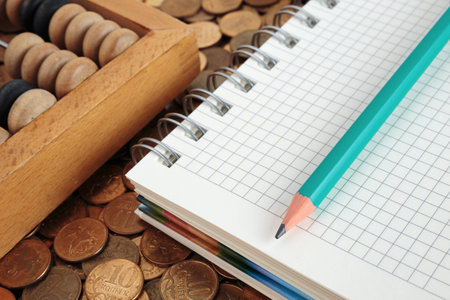Notepad with pencil and abacus on a pile of coinsの写真素材