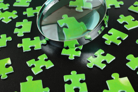Green puzzles and magnifying glass on a black leather backgroundの写真素材