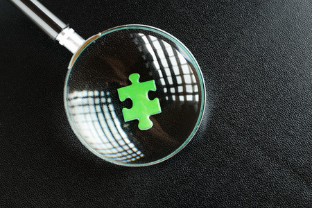 Green puzzles and magnifying glass on a black leather backgroundの写真素材