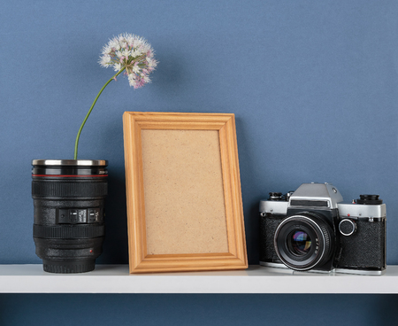 Decorative vases with flower and old camera on white  shelf on blue wallpaper background