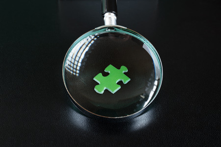 Green puzzles and magnifying glass on a black leather backgroundの写真素材