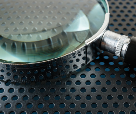 Magnifying glass on a metallic background with perforation of round holesの写真素材