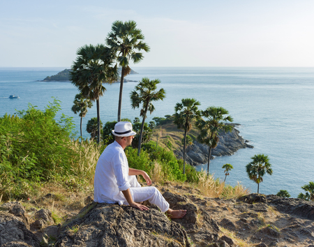 a young man sitting on a rock and looking at the sunset of Phuketの写真素材