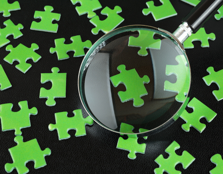 Green puzzles and magnifying glass on a black leather backgroundの写真素材
