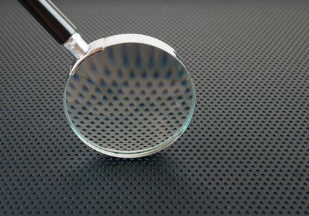 Magnifying glass on a metallic background with perforation of round holesの写真素材