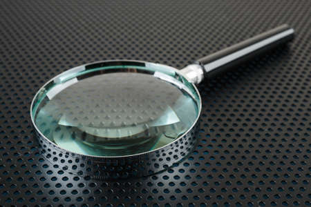 Magnifying glass on a metallic background with perforation of round holesの写真素材