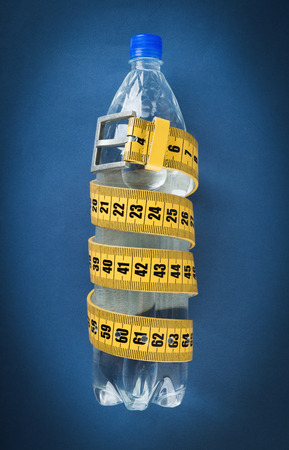Yellow meter belt slimming and a bottle of water on a blue backgroundの写真素材
