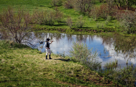 Man in black hat with a stick standing on the river bank