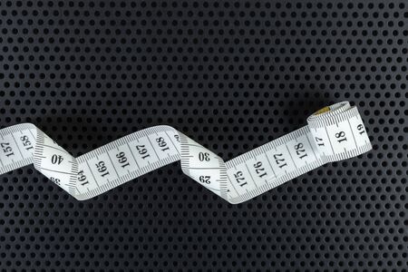 Curved white measuring tape on black background  perforated