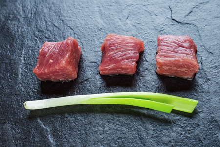 Three cubes of meat and green onions on the black stone tableの写真素材