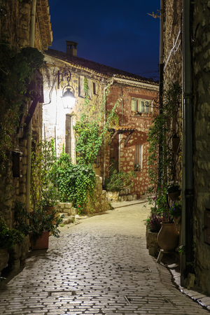 Narrow cobbled street with flowers in the old village Tourrettes-sur-Loup at night, France.の写真素材