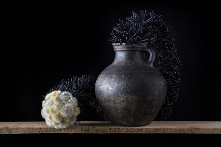 Still life with an old clay jug and dandelions isolated on black backgroundの写真素材