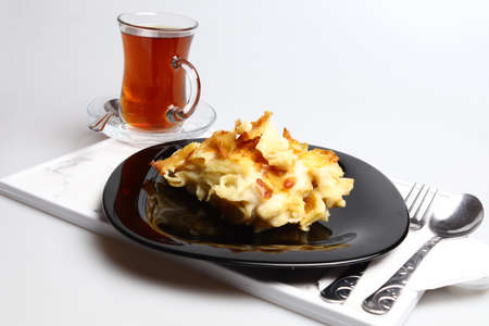 Delicious baked cake and hot tea in black porcelain plate on white background