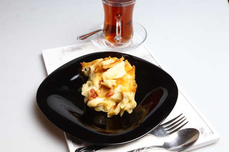 Delicious baked cake and hot tea in black porcelain plate on white background