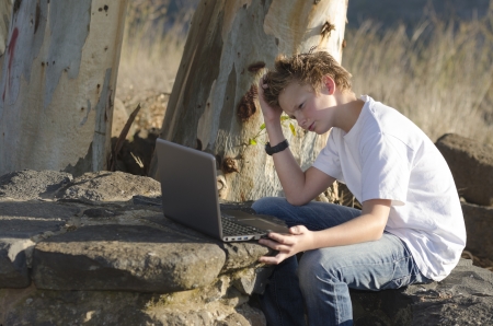 Thoughtful teenager sits on nature with laptopの写真素材