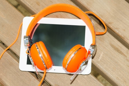 White tablet PC and orange headphones on the wood benchの写真素材