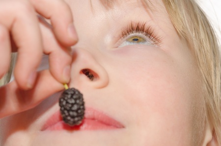 Closeup portrait of cheerful girl, holding in hand and eating mulberry fruitの写真素材