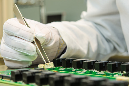 Female hand holding tweezers and installing connector on PCB in turnkey solutions high-tech...