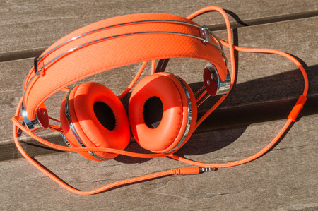 Vibrant orange wired headphones on the wooden benchの写真素材