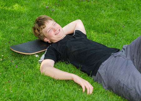 Laughing guy relax on skateboard in park grass and rest after an active leisureの写真素材