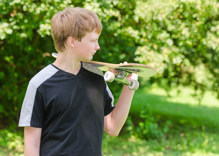 Profile portrait of young skater stand in the park and holding a skateboard on shoulderの写真素材