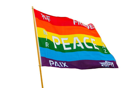 Waving rainbow varicolored pacifist flag with multilingual peace text wind fluttering isolated on white backgroundの写真素材