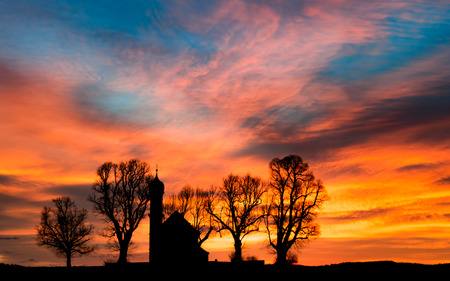Early morning sunrise dawn with black silhouette of small church or chapel and bare trees on colorful cloudy flaming sky backgroundの写真素材