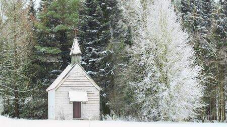 Peaceful winter view of little snow-capped rural wooden church on snowfield glade in frozen forestの写真素材