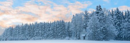 Panoramic landscape of snowbound forest with frosty small church unter morning sunrise cloudy skyの写真素材
