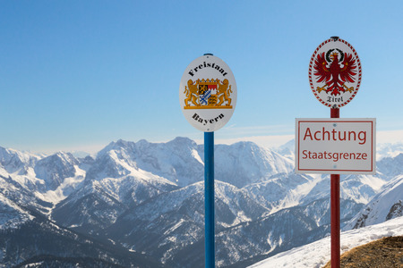 State boundary between Germany and Austria on top of Alpine mountain ridge. Sgnboards with the coat of arms of free state Bavaria and Tyrol and words "Warning: National Border".の写真素材