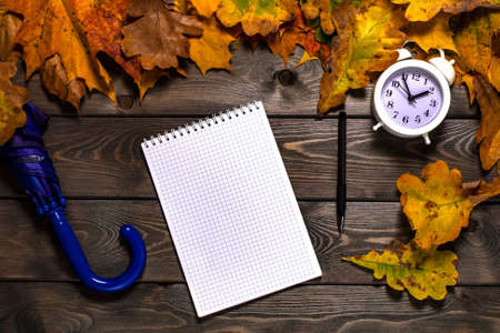 autumn composition with yellow leaves, Notepad, alarm clock and umbrella on a textured wooden tableの写真素材