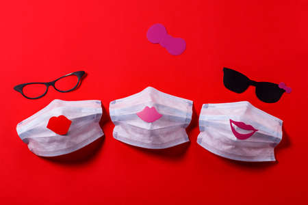 the concept of friendship. medical face mask with glasses and lips of girls made of cardboard on a background of red texture paper. virus protectionの写真素材